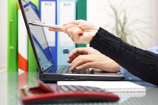 Photo of hands typing on computer, pointing at document